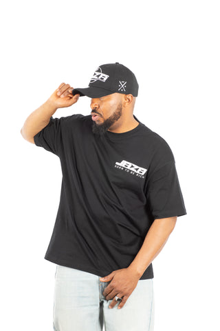 „Seitliche Aufnahme eines Models im schwarzen JAZA T-Shirt mit weißem Brustprint, kombiniert mit schwarzer JAZA Cap.“